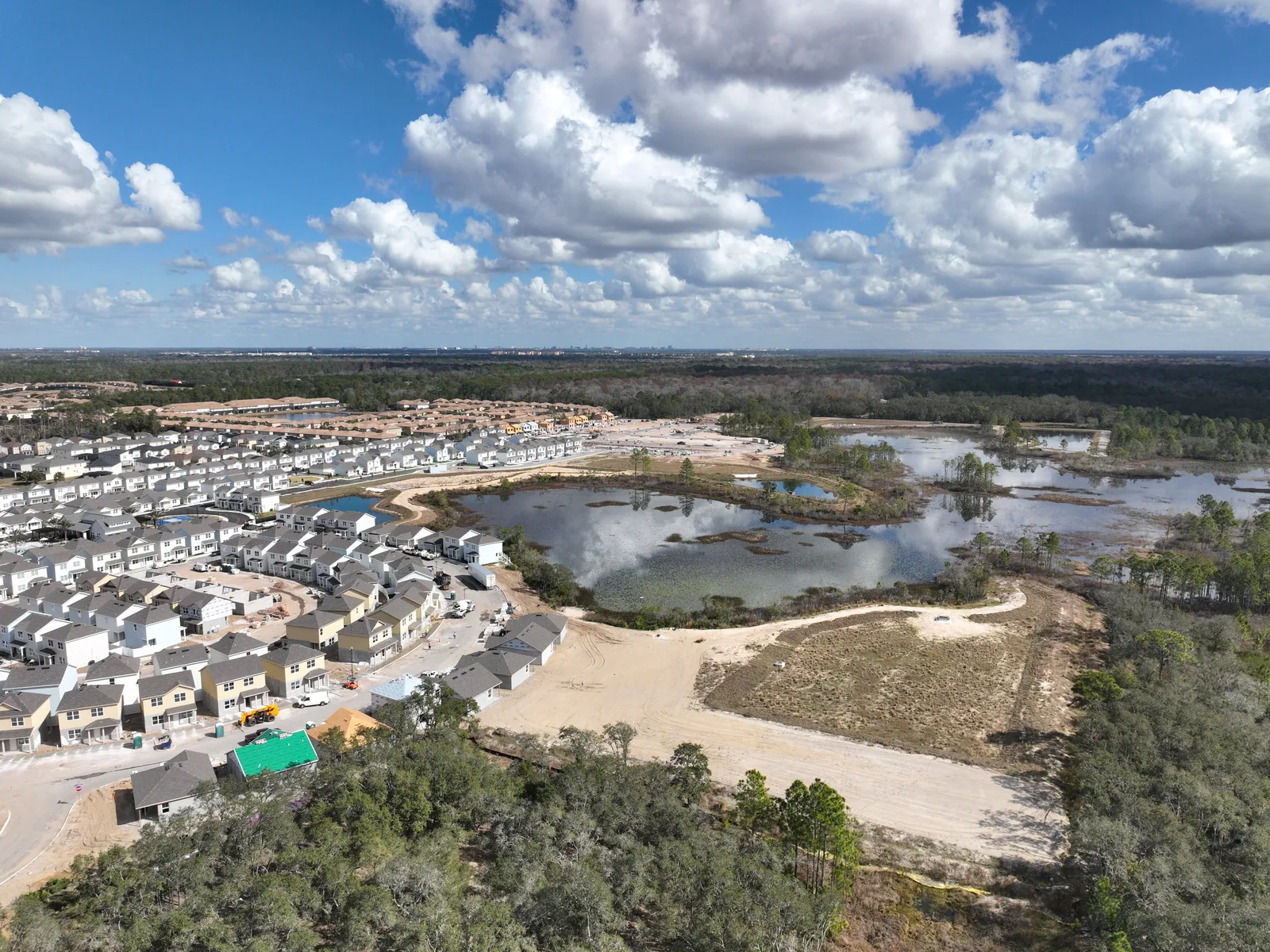 Wide aerial photograph of the same master-planned residential community at a later phase of construction, showing expanded finished housing, additional paved roads, completed retention ponds, and a reduced footprint of active grading compared to the earlier capture.